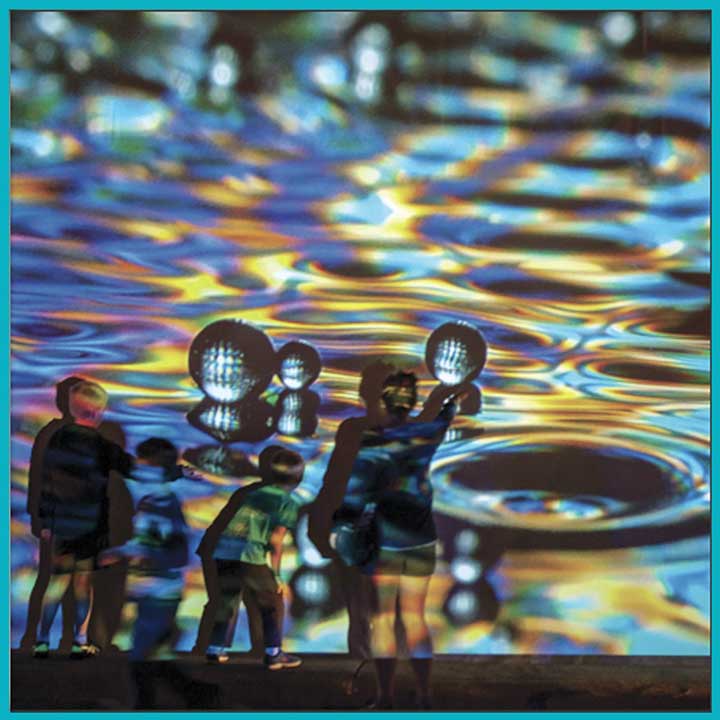 Photo of a group of children in front of a projected photo of iridescent water drops