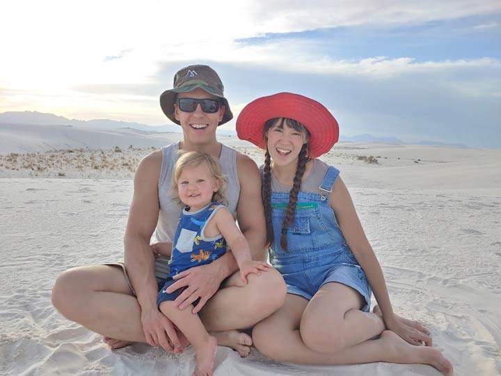A photo of Melissa with her husband and toddler sitting and smiling at White Sands, NM.