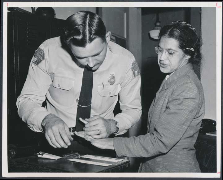 A black and white photo of Rosa Parks being fingerprinted by a sheriff.