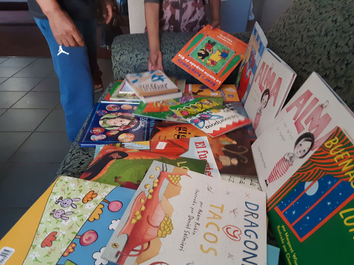 Photo of a table full of children's books. A person is picking up one of the books.