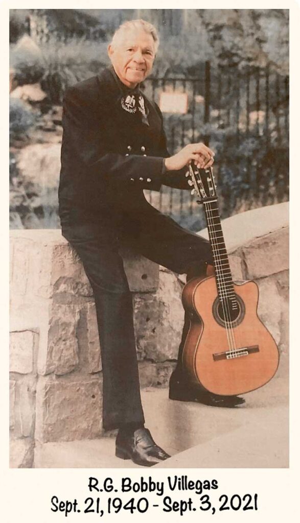Photo of Bobby Villegas standing on concrete steps, holding his guitar. It reads "R. G. Bobby Villegas, Sept. 21, 1940-Sept. 3, 2021"