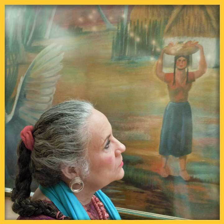 Photo of Denise Chávez in front of a mural depicting a woman carrying a basket of food on her head
