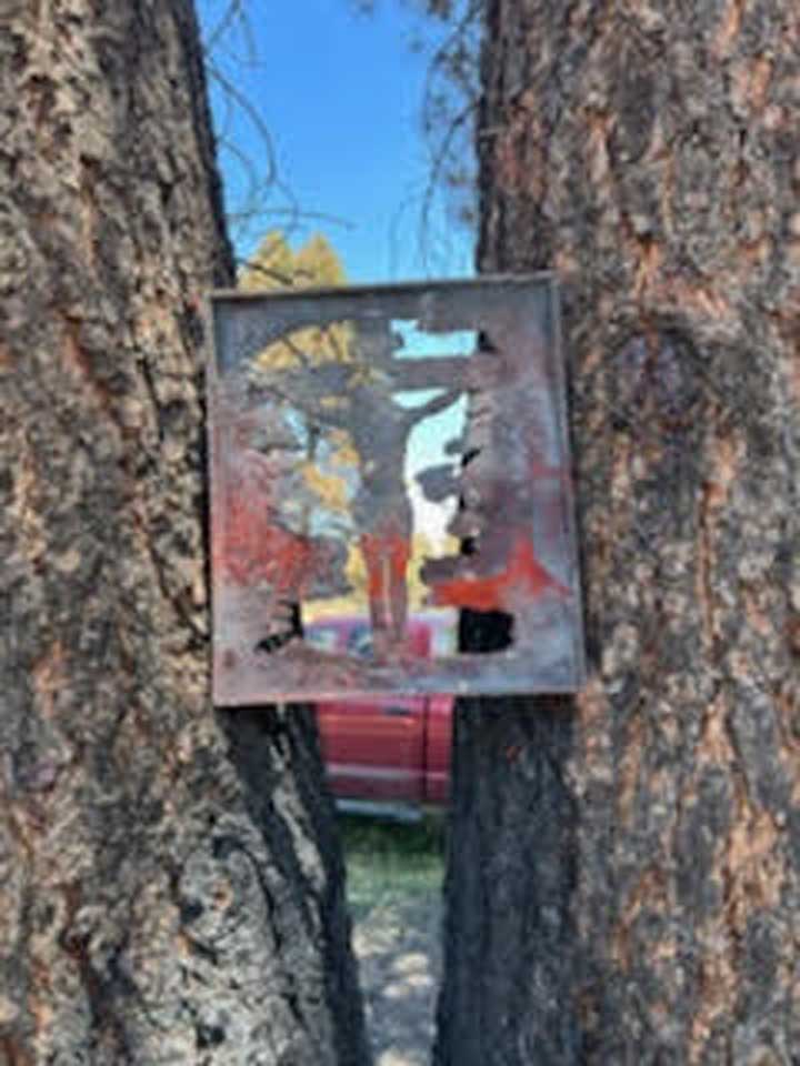 Photo of a metal cutout artwork of the crucifixion, held between two trees.