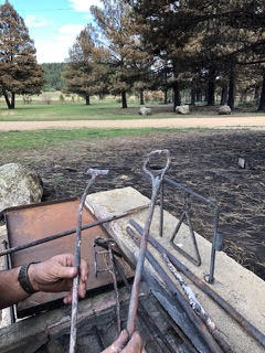 Image of hands holding branding irons in the middle of a charred field/yard