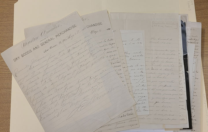 Photo of a fanned-out stack of handwritten letters from 1890 on a table.