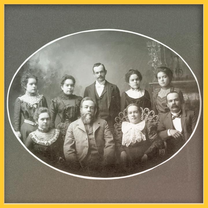 Black and white studio portrait of the Amador Family, the parents are in the middle surrounded by their 7 children.