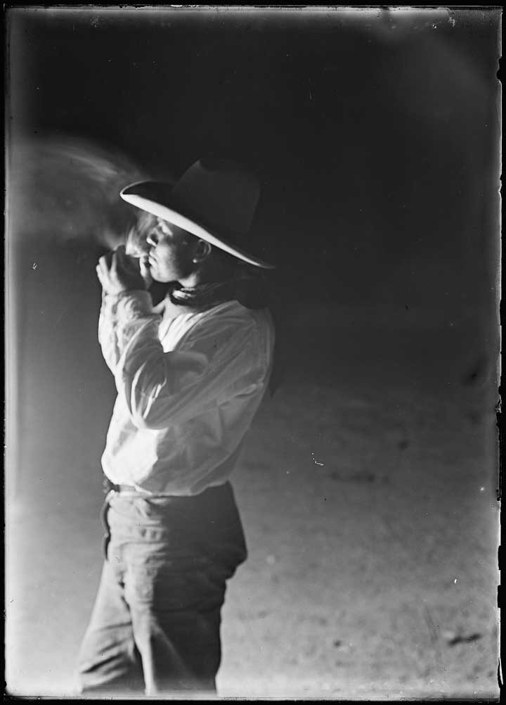 Black and white film photo of a cowboy smoking a cigarette at night. The edges of the photo are ragged.