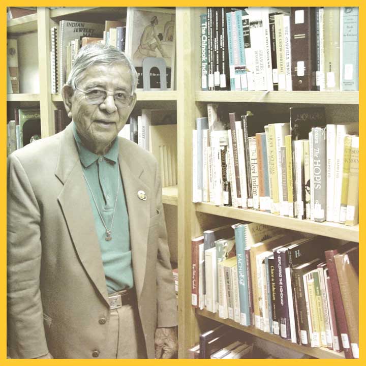 Photo of Dr. Joe Sando posing with bookshelves in a library