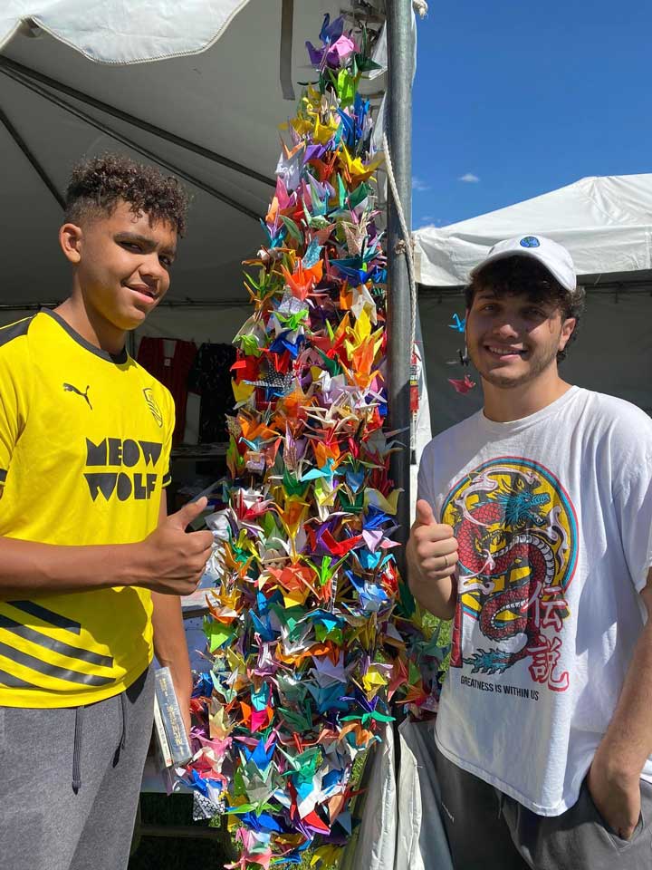 Hakim Bellamy's sons, Kaylem & Max, standing next to a garland of paper cranes and giving a thumbs up.