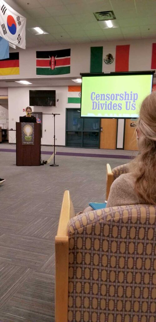 A photo of a woman at a podium giving a presentation. A screen next to her reads "Censorship Divides Us"