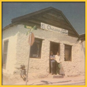 A photo of a white stone building with a hand-painted sign above the door that reads "El Chicano Youth Center." Two people are standing in the doorway.