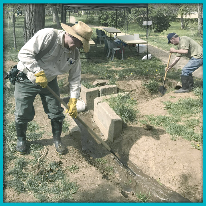 Two men working together to clean out an acequia also known as an irrigation canal used to water crops.
