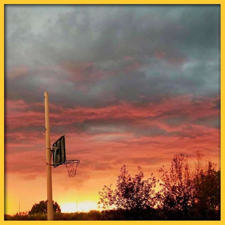 Photo of a vibrant sunset with basketball hoop in the foreground