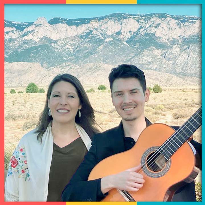 Photo of Rosalia and Estevan Pacheco in front of the Sandia Mountains. Estevan is holding a guitar