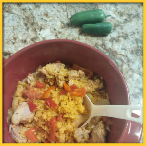 Photo of a spoon in a bowl of arroz con pollo with a couple of green peppers in the background.