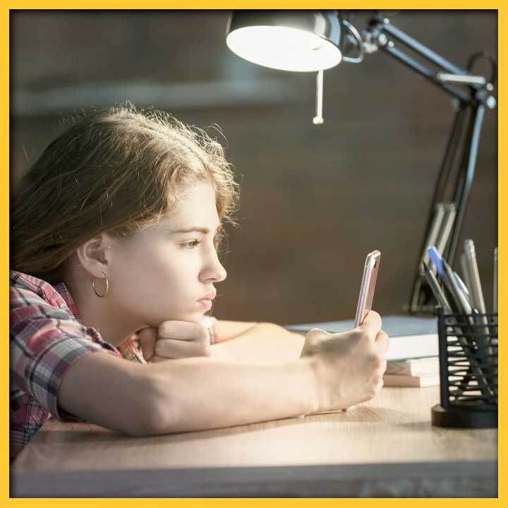 Girl leaning on desk looking at cellphone.