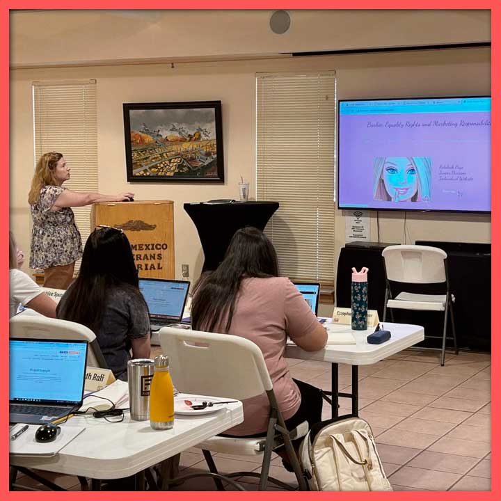 Photo of Amy Page leading a teacher workshop. The screen at the front has a photo of Barbie and reads, "Barbie: Equality Rights and Marketing Responsibilities"