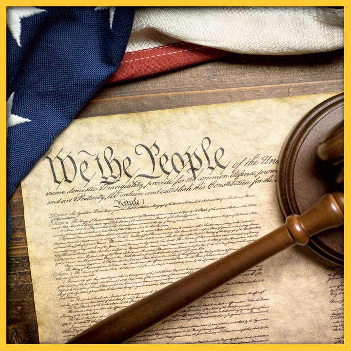 Photo of the US Constitution on a desk with a US flag and a gavel. "We the People" is clearly legible.