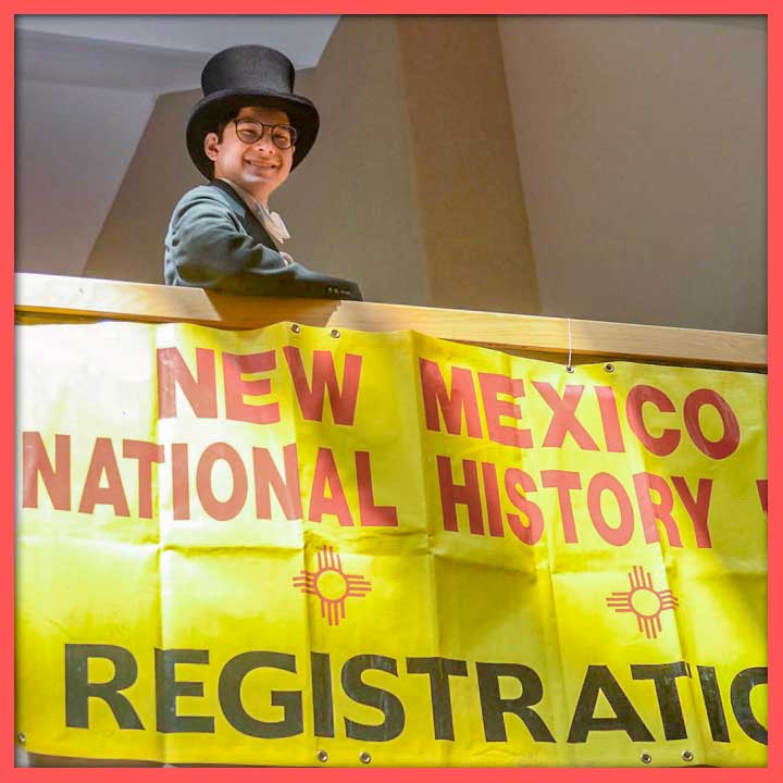 National History Day student dressed in a top hat posing with the registration sign.