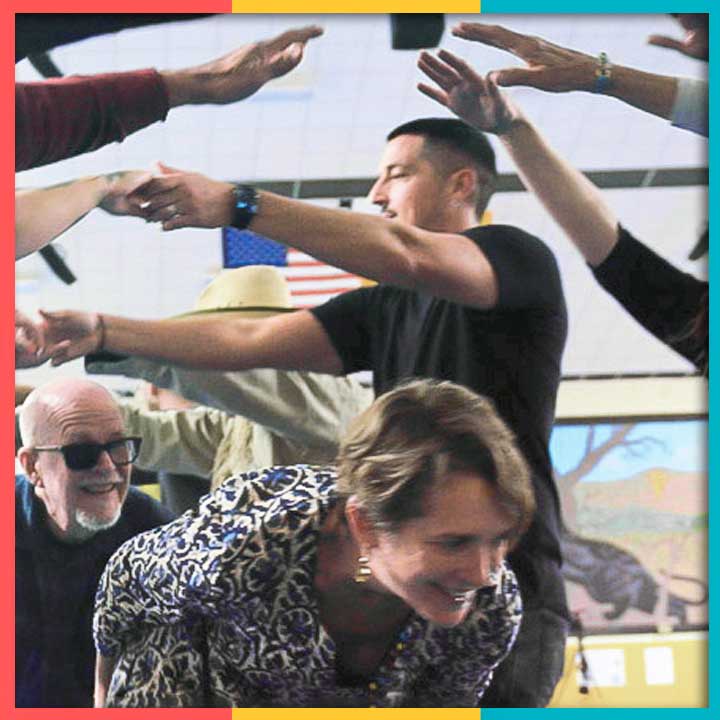 A line of people forming a tunnel with their hands with two people crouching through the tunnel