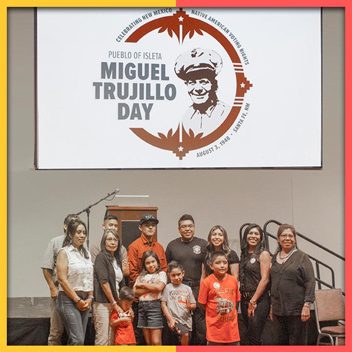 Photo of a group of people gathered in front of a podium. Above them is a sign that says "Miguel Trujillo Day" with an image of Miguel Trujillo