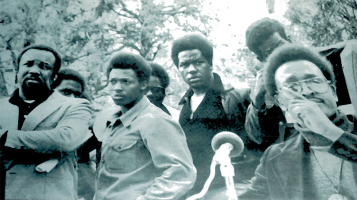 Photo from the 1960s/70s of Dr. Bailey in front of a microphone with 6 men in the background, including Dr. Charles Becknell, Sr.