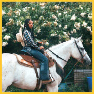 Photo of a teenage boy sitting on a horse with a cowboy hat hanging on his back